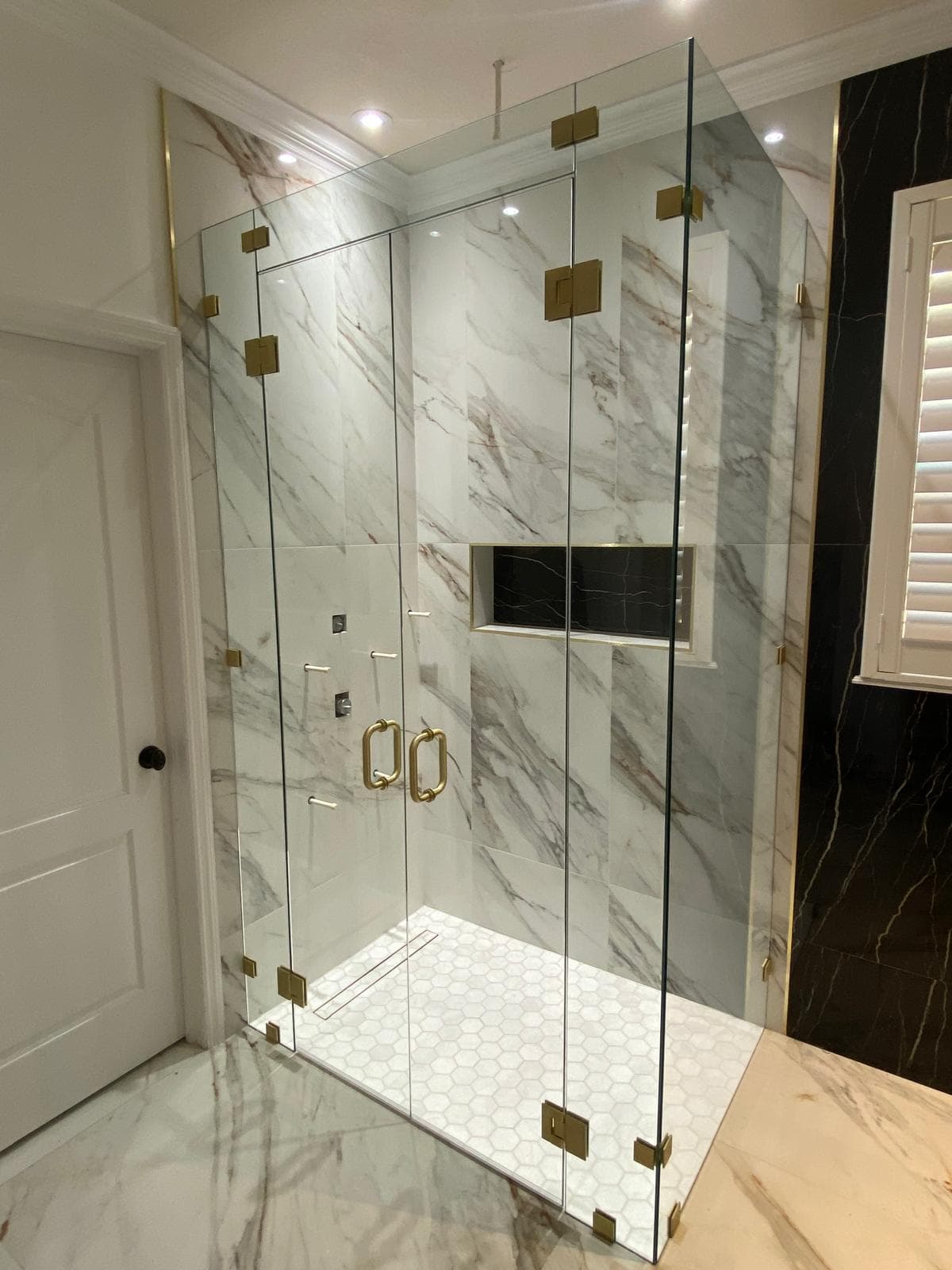 Frameless shower enclosure with brushed brass hardware on Calacatta marble