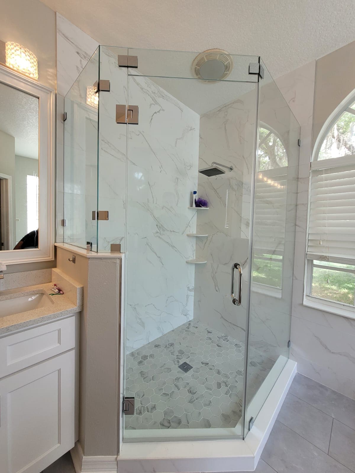 Frameless neo-angle shower enclosure in white marble with chrome hardware
